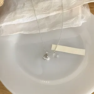 Détail du pendentif coquillage argenté et du collier en perles de cristal sur plat