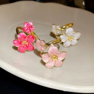 Close-up of delicate gold flower rings with pink and white enamel petals on a plate.