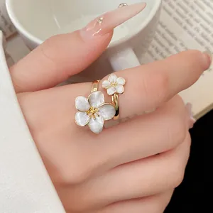 Close-up of vintage-style gold ring with two white enamel flowers worn on finger