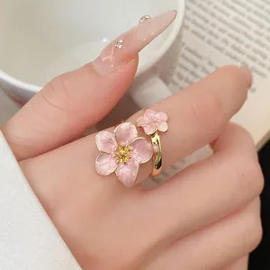 A detailed close-up shot of an elegant pink enamel flower ring worn on a finger
