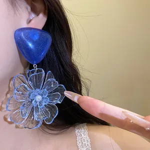 Detailed macro view of large transparent blue resin flower earrings with silver needle