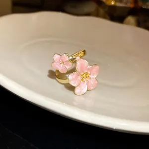 Close-up of a vintage-style gold ring with pink enamel cherry blossom flowers.