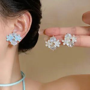 Close-up van elegante bloemige zirkoon oorknopjes in blauw en wit op een model.