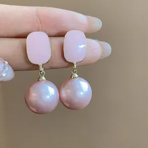 Macro detail of elegant pink enamel square stud earrings with dangling pearl drops