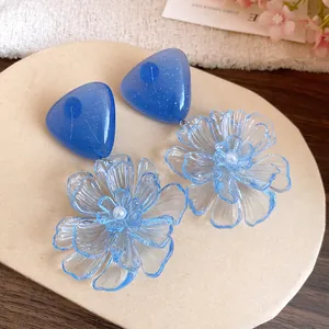 Close-up detail of blue resin triangle stud earrings with translucent flower pendants