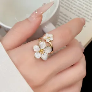 Close-up of elegant gold-plated open ring with white enamel cherry blossom flowers