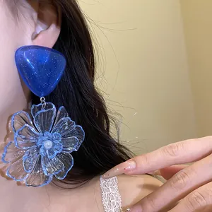 Close-up of blue resin flower drop earrings with silver needle on an Asian model