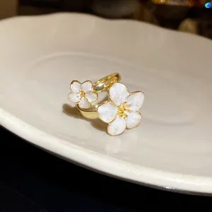 Detail of gold adjustable ring featuring delicate white enamel flower motifs