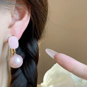 Macro detail view of elegant pink enamel stud with round pearl drop earring on model ear