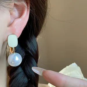 Close-up detail of French style square creamy enamel and large pearl drop earrings on ear
