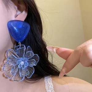 Detailed close-up showing large blue resin flower pendant earrings worn by a model