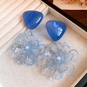 Detail view of blue resin triangle studs and transparent flower drop earrings with pearls
