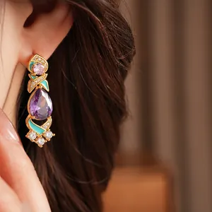 Close-up of vintage palace style gold earring with purple teardrop zircon and green enamel
