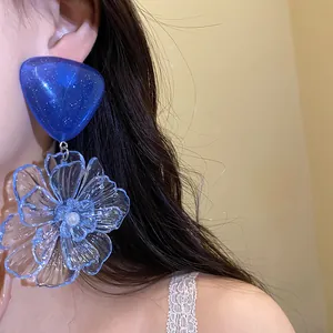 Close-up view of blue resin flower drop earrings featuring a sparkling triangle stud