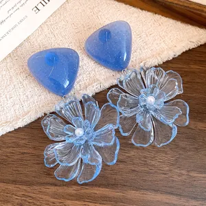 Close-up of blue resin triangular earrings featuring large clear flower pendants