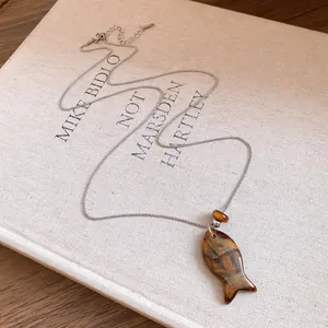 Vue détaillée du collier pendentif poisson en résine avec chaîne argentée sur livre