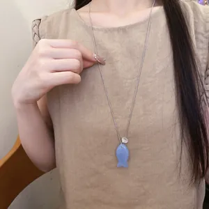 Détail d'un long collier argenté avec un pendentif en forme de poisson en résine bleue