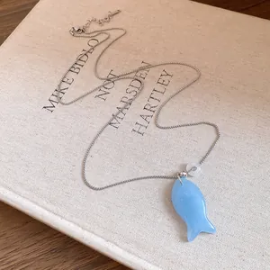 Détail d'un collier avec pendentif poisson en résine bleu clair sur un fond de livre d'art.