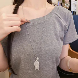 Détail rapproché d'un collier pendentif poisson en résine blanche porté sur un t-shirt gris