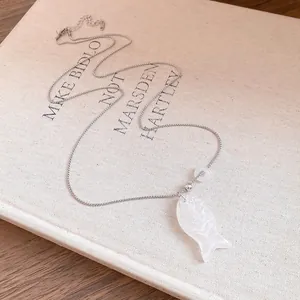 Détail d'un collier pendentif poisson en résine blanche sur une couverture de livre.