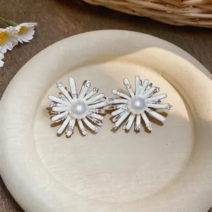 Close-up of white flower stud earrings with a central pearl and tiny rhinestones.