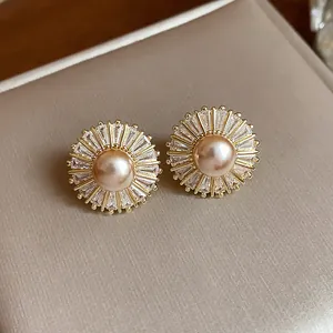 Close-up of elegant sunburst zircon pearl stud earrings with champagne pearls and gold finish