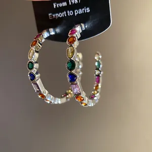 Detailed close-up of C-shaped earrings with colorful sparkling zircon stones.