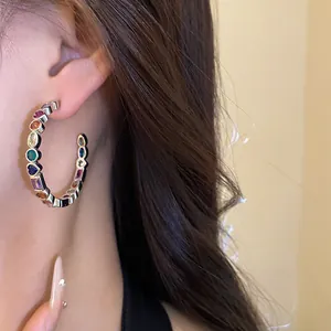 Detail view of a C-shaped silver earring with vibrant colorful zircon stones.