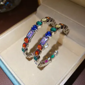 Close-up of C-shaped silver earrings with vibrant multi-colored geometric zirconia stones
