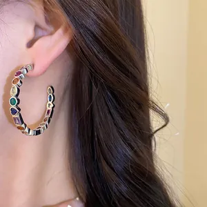 Detail showing multi-colored zircon geometric C-shaped hoop earring on model's ear