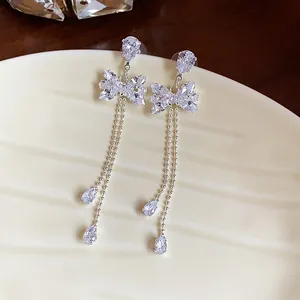 Close-up of elegant silver zircon bow earrings with long shimmering tassels on a dish