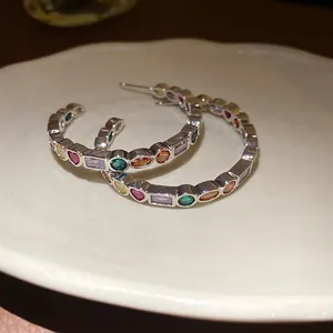 Detail view of silver C-shape hoop earrings featuring colorful geometric zircons