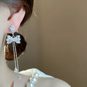 Detailed close-up of sparkling zircon bow-knot tassel earrings on model with pearls