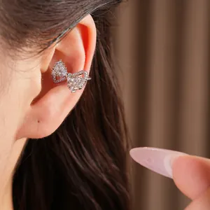 Detailed view of a silver bow ear cuff with sparkling zircons worn on a model's ear.
