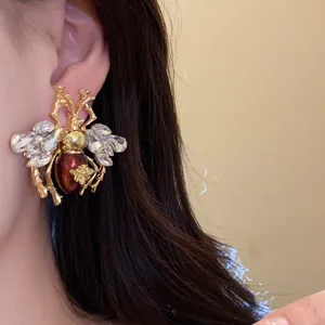 Close-up detail of luxury vintage insect earring with crystals and red enamel on ear