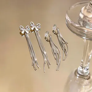 Detailed view of silver bow zircon earrings with long tassel chains on golden surface.