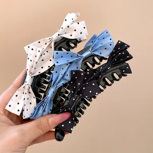 Hand holding a set of three polka dot bow banana hair clips in black, blue and white.