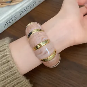 Gros plan d'un bracelet élastique en résine marbrée rose irrégulière avec accents dorés