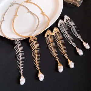 Detailed view of oversized fishbone pendants with pearls in gold and silver finishes.