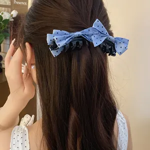Detail view of a stylish light blue polka dot bow banana clip worn on dark hair