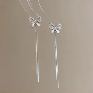 Detailed view of silver bow stud earrings with sparkling zircon and long tassels