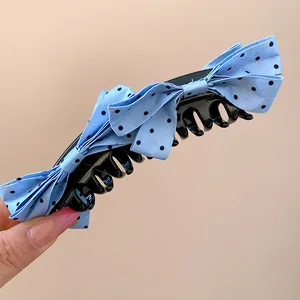 Detail close-up view of blue polka dot fabric bow hair banana clip held by hand
