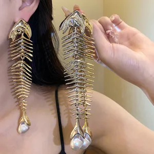 Detailed view of oversized gold fishbone earrings with sparkling crystals and pearls.
