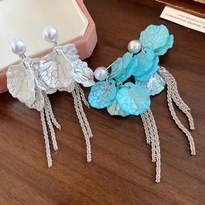 Close-up of elegant pearl petal tassel earrings with long silver chains on wooden table.