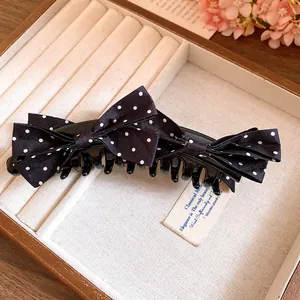 Elegant close-up of a black and white polka dot bow banana hair clip in a box