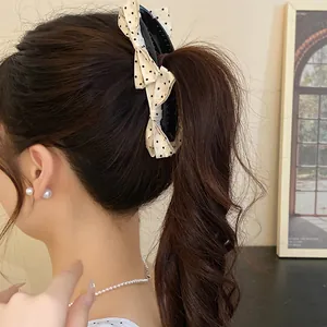 Close-up of a cream bow banana clip with black polka dots on a ponytail