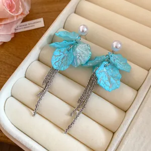 Close-up of light blue petal drop earrings with pearl studs and silver tassels