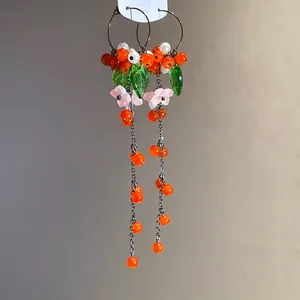 Detailansicht langer Quastenohrringe mit orangefarbenen Perlen und Harzblumenblättern