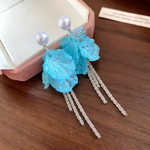 Close-up of blue petal tassel earrings with white pearl studs on a wooden background