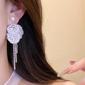 Close-up detail shot of elegant white petal earrings with long silver tassel chains on ear